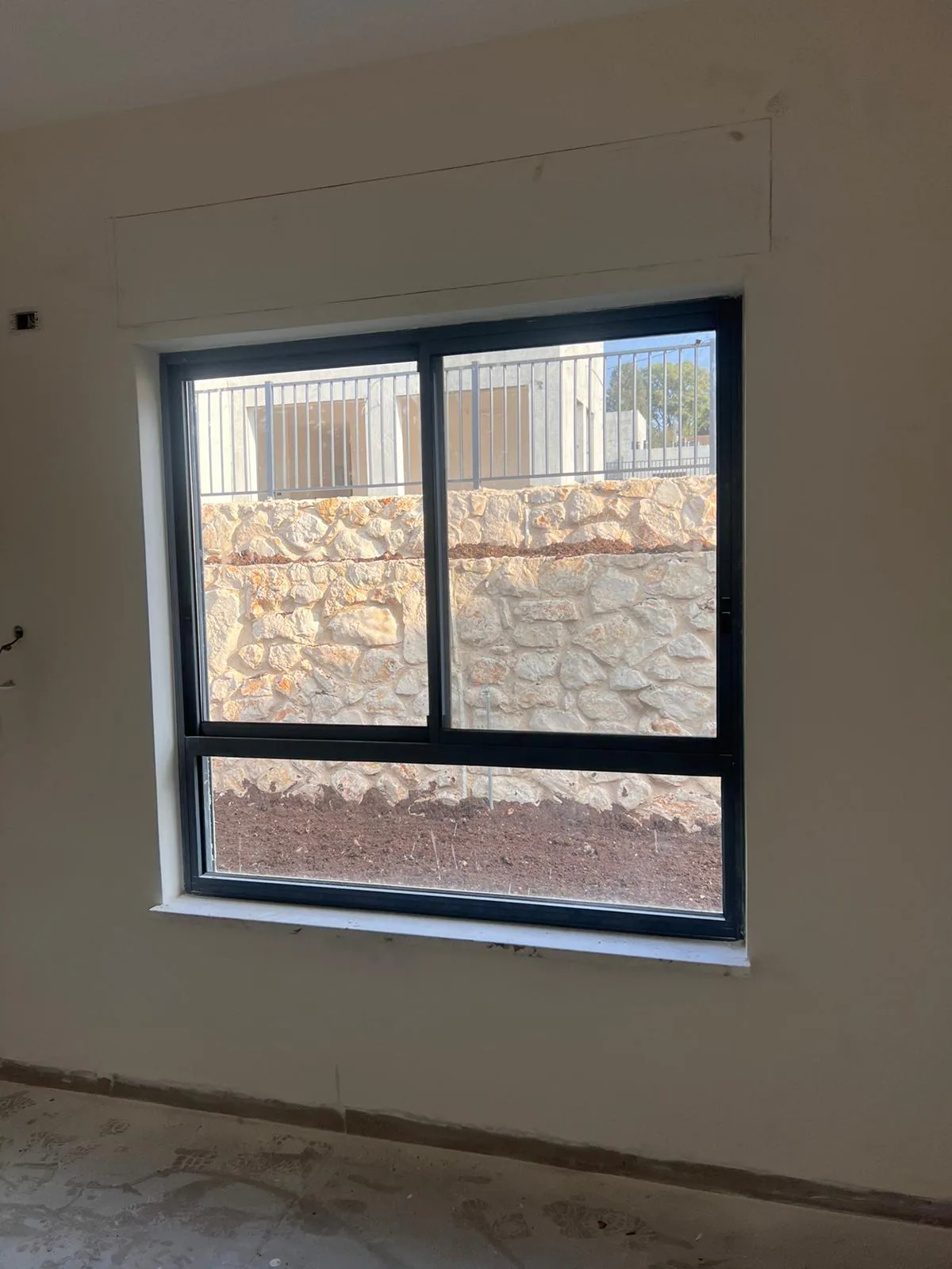 חלון הזזה שחור בחדר לא גמור, מול קיר אבן וגינה